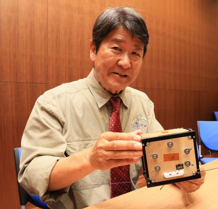 Takao Doi sostiene un modelo del satélite artificial de madera, LignoSat.