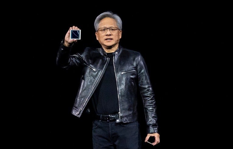 Hombre con una chaqueta de cuero y gafas sosteniendo un chip de computadora en un escenario de conferencia.