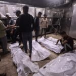 Un grupo de hombres palestinos atiende a varios cuerpos envueltos en blanco en el suelo de una morgue en Gaza.