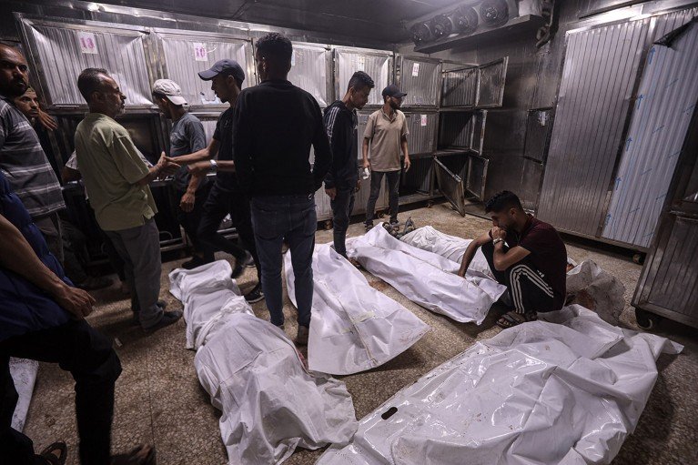 Un grupo de hombres palestinos atiende a varios cuerpos envueltos en blanco en el suelo de una morgue en Gaza.