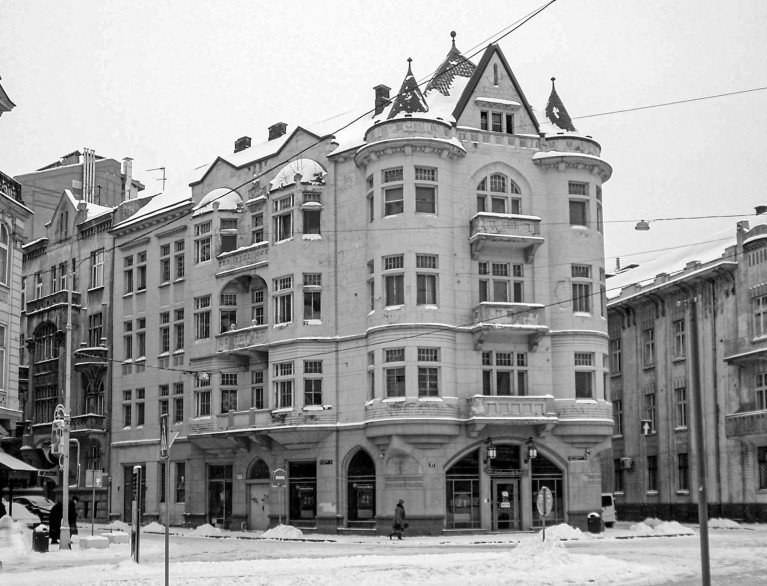Un camino cubierto de nieve frente a un edificio de cuatro plantas con torrecillas y balcones